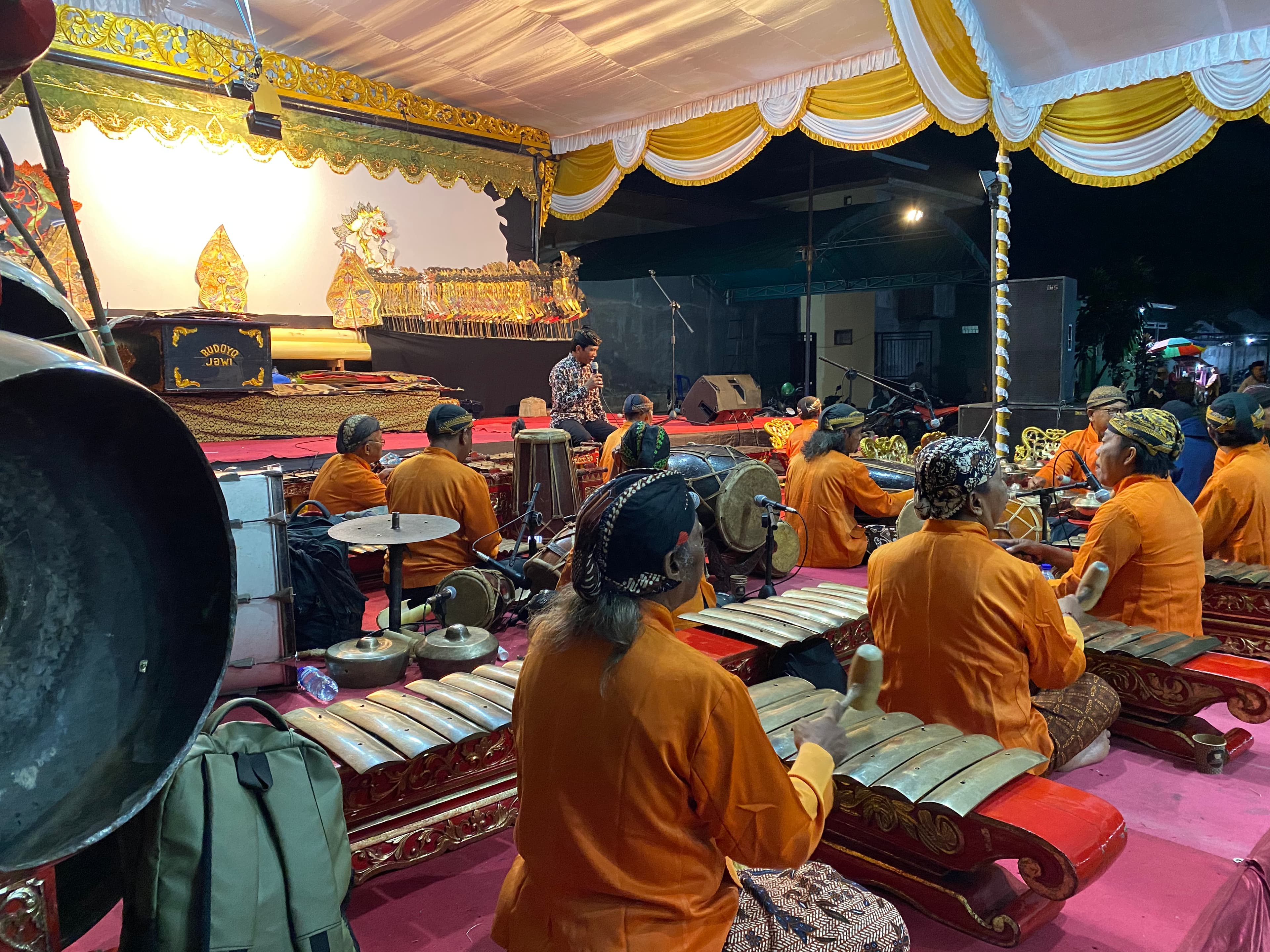 Pertunjukan wayang kulit di balai desa oleh para seniman diiringi musik tradisional.